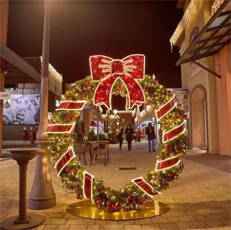 Large lit commercial Christmas wreath with a red bow mounted in a shopping centre concourse