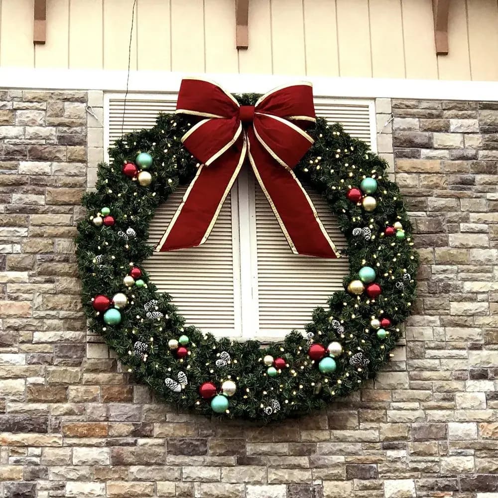 Decorated commercial wreath with ornaments and a red bow mounted on a stone building facade