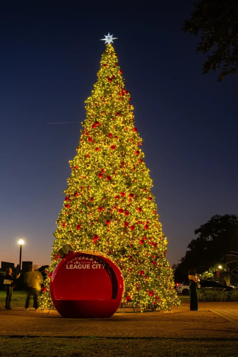 Giant commercial Christmas tree lighting a downtown square at night